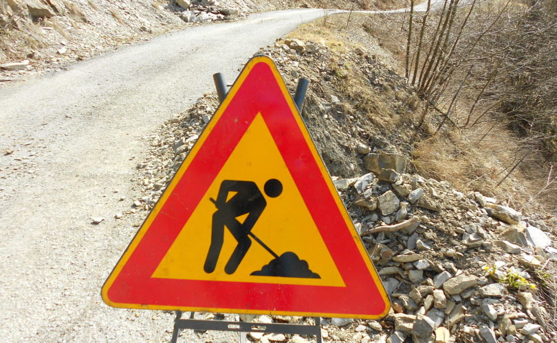 Cartello stradale di lavori in corso a lato di una strada sterrata